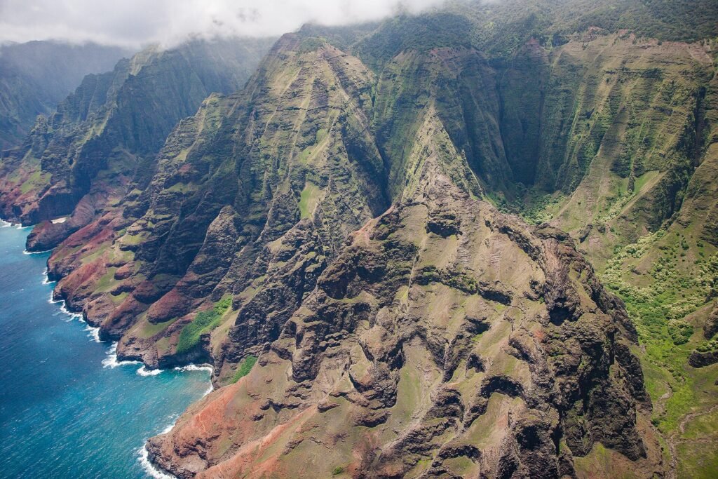 Aerial view of the Na Pali Coast ridgelines and turquoise water seen on a Kauai helicopter tour